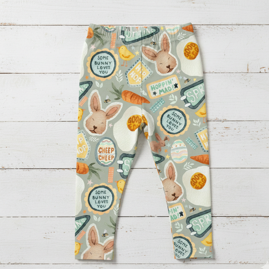 baby and children's sage green
 leggings with Easter-themed design featuring bunnies, eggs, and carrots on a wooden surface.